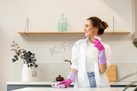 一位戴橡胶手套的年轻貌美的女士拿着一瓶洗涤剂，微笑着擦拭厨房的台面。打扫房子的概念。清洗产品.