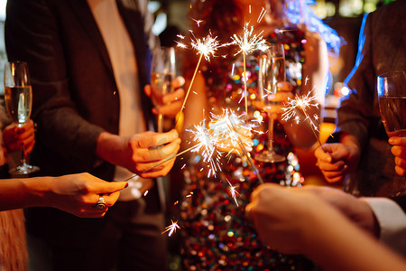 手里拿着闪闪发光的火花。一群快乐的人在聚会上手握火花.年轻的朋友们在夜总会里碰杯香槟.庆祝活动、人与假日概念.