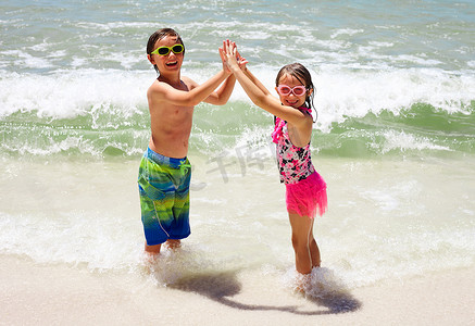 两小孩子摄影照片_快乐的小孩子们手牵着手在海滩上