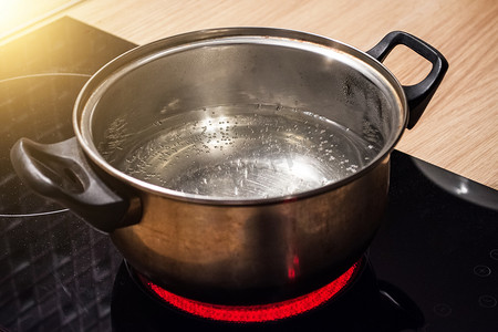 金属锅与沸腾的水在电磁炉红色热板.