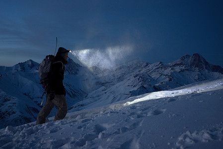 勇敢的夜探险者爬上高高的雪山, 用车头灯照亮道路。极端远征。滑雪之旅。滑雪板承诺攀登冬季斜坡。穷乡僻壤