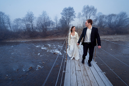 Happy wedding couple laughing and having fun on the suspension bridge in mountains