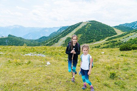 在美丽的夏日里，孩子们在奥地利的阿尔卑斯山中徒步旅行，休息在岩石之上，欣赏高山的壮丽景色。与孩子一起积极享受家庭假期。户外运动快乐健康.
