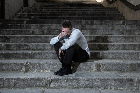 年轻的商人哭着放弃失落在忧郁中坐在街头的楼梯上痛苦的情绪痛苦, 悲伤的精神健康概念照片