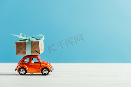 玩具红色汽车的侧视图与圣诞节礼物箱子骑马在白色表面在蓝色背景