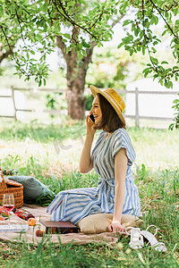 公园里，一个微笑的女人在靠近食物和葡萄酒的地方用手机交谈时的侧影 