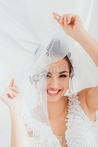 新娘穿着婚纱，手持面纱，凝视着靠近白布的相机的选择性焦点 