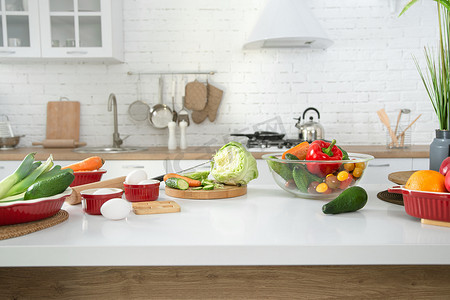 囤生活用品摄影照片_现代时尚厨房内部的蔬菜和水果在桌子上。明亮的白色厨房，有家用物品。健康生活方式的概念.
