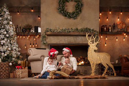 圣诞花环摄影照片_照片上的父母带着儿子在壁炉边，鹿带着花环在房间里