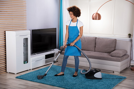 年轻女清洁工在起居室里用吸尘器清扫地毯