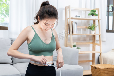 Woman in a gym clothes uses a centimeter strap to measure her circumference thin waist, Thin waist female, Health care concept and weight control, Sports waist, Healthy lifestyle, Physical activity.