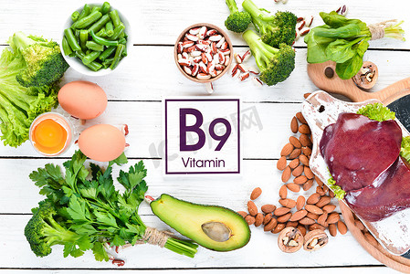 木制摄影照片_含有天然维生素B9的食物：肝脏、鳄梨、花椰菜、菠菜、欧芹、豆类、坚果，在白色木制背景上。顶部视图.