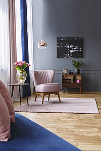 粉红色的椅子旁边的桌子与鲜花在典雅的客厅内部与黑色海报。真实照片