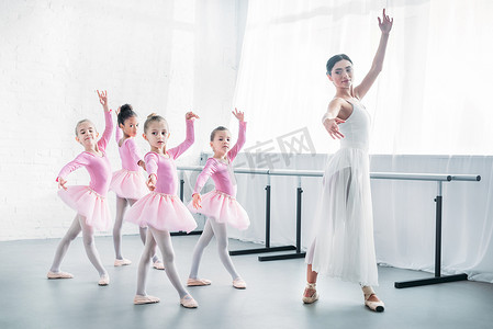 年轻的老师练习芭蕾与可爱的孩子粉红色短裙裙