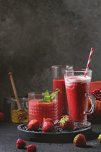 三种不同的红果浆果西瓜, 草莓, 覆盆子, 石榴鸡尾酒或冰沙杯中的冰, 薄荷和配料上面的黑色纹理表。食物静物.