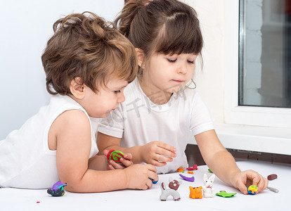 两小孩子摄影照片_两个可爱的小孩子在托儿所玩着五颜六色的粘土造型。创意儿童在家中成型。男孩和女孩玩橡皮泥或面团.