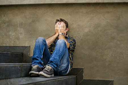 年轻的悲伤和绝望的男子坐在户外的街道楼梯感到焦虑和沮丧痛苦的哭泣被抛弃在失业和破碎的心的概念