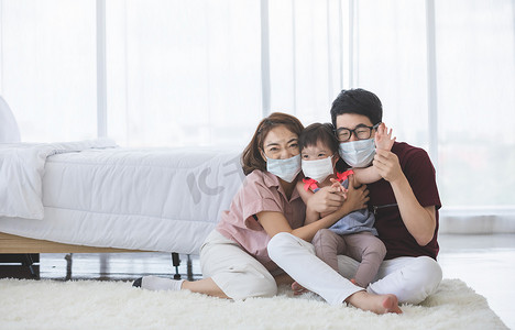 为了防止PM2.5灰尘、烟雾、空气污染和COVID-19，亚洲家庭头戴口罩，站在客厅里看着相机。保健概念.
