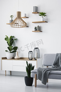 木制吊灯, 白色墙壁上的简单架子和一个在单色起居室内部的斯堪的纳维亚餐具柜上的植物