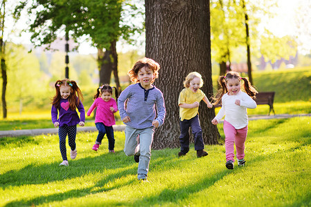 许多年幼的孩子微笑着沿着公园的草地奔跑。.