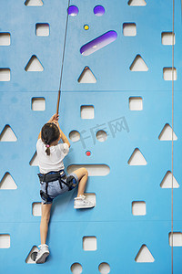 一个勇敢的小女孩穿着安全绳在室内爬墙以锻炼自己的力量的背影