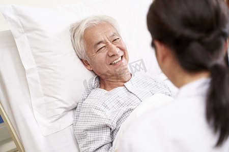 年轻的亚洲医生在临终关怀的病床边与老年病人交谈