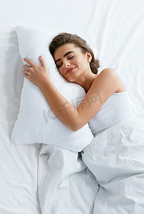 健康的睡眠。女人睡在白色的床上用品上, 带软枕头, 床垫配毯子。高分辨率.