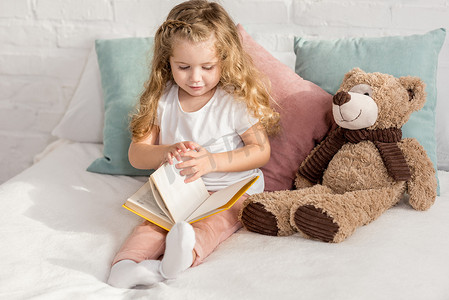 可爱的孩子玩泰迪熊和阅读书籍在床上的儿童房