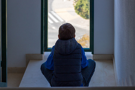 孤独的男孩坐在窗前的楼梯上