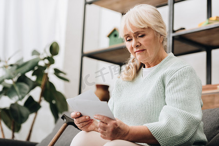 悲伤的退休妇女拿着照片在客厅里
