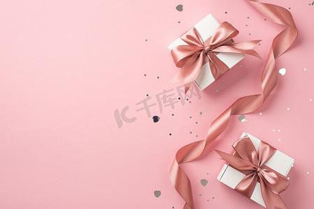 confetti摄影照片_Top view photo of white gift boxes with pink bows curly ribbon silver sequins and heart shaped confetti on isolated pastel pink background with copyspace