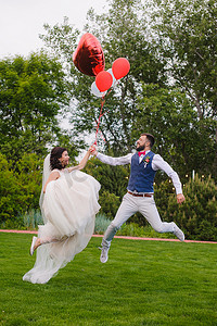 愉快的已婚夫妇跳跃与红色气球