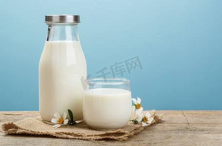 一瓶乡村牛奶和一杯牛奶，放在蓝色背景的木制桌子上，是美味、营养和健康的奶制品