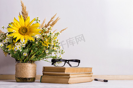 放书摄影照片_白板上的花瓶里放着书、眼镜、记号和一束鲜花。教师节和9月1日的概念。复制空间.