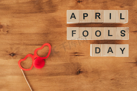 被安排的木立方体的上部看法在4月傻瓜天字体与党镜片和小丑鼻子在木桌上, 4月1日假日概念