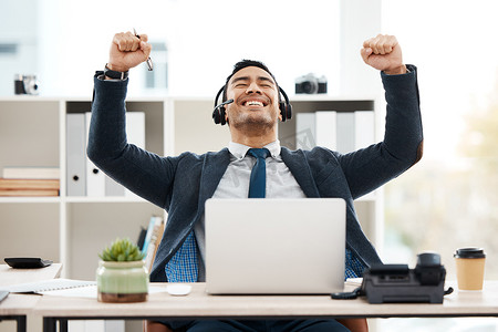 laptop摄影照片_a young male call center agent cheering while using a laptop in an office at work.