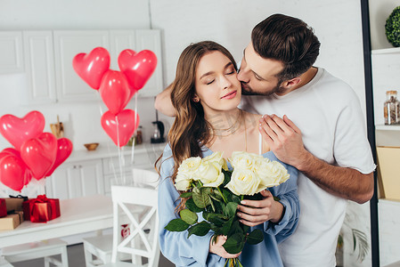 快乐的女孩拿着玫瑰花束闭着眼睛, 而男友亲吻脸颊和拥抱女朋友