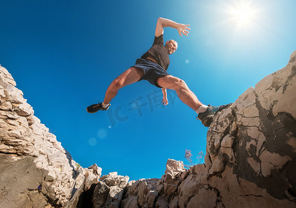 在晨跑中，活跃的高山长跑者笑着跳过裂隙悬崖。身材瘦小的人活动一个广角的概念形象.