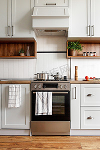 烹调摄影照片_时尚的灰色厨房内饰与现代门和不锈钢家电在新家。斯堪的纳维亚风格的厨房设计。绿色植物装饰, 火炉, 烟囱。烹调食品