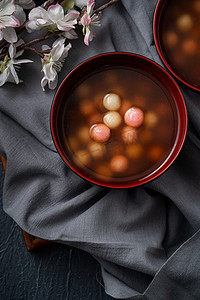 饺子汤圆摄影照片_红白相间的汤圆（汤圆，糯米饺子球）配上甜糖浆汤，放在蓝色桌子背景的碗里，作为冬至佳肴.