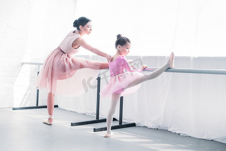 年轻的芭蕾舞老师看着小学生伸展芭蕾工作室