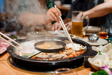 煮火锅摄影照片_人们在中餐馆吃火锅晚餐。用筷子吃饭, 用煮汤煮生的食物块.