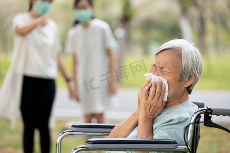 亚洲老年生病妇女流鼻涕，打喷嚏发烧，感染流感症状，眼镜蛇-19，大肠癌，两个戴面具的人，避免与病人接触，保持距离