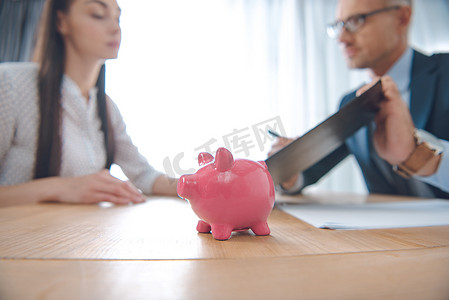 与粉红小猪银行在桌面上的保险代理和客户的选择性焦点