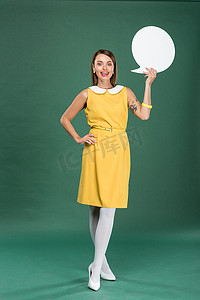 美丽时尚的女人在黄色礼服看着相机, 并举行在绿色背景的演讲泡沫