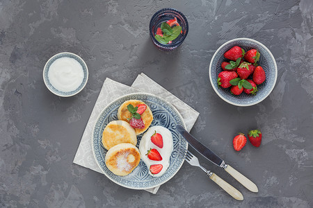 在灰色背景下, 早餐或午餐用酸奶奶油和草莓做的干酪煎饼。健康食品概念。顶部视图