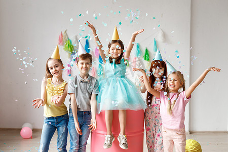 不同活动摄影照片_可爱的孩子们一起玩, 扔五颜六色的五彩纸屑, 戴圆锥帽, 在生日聚会上玩, 在不同的游戏中一起玩耍, 花时间在装饰的房间里。儿童与活动概念