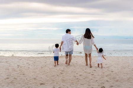 亚洲家庭节日快乐，父亲、母亲、儿子和女儿欢欢喜喜地一起走在夏日夕阳的海面上。假日、夏天和假期，一家人在海滩上愉快地旅行.