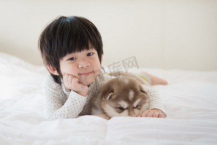 哈士奇摄影照片_孩子和西伯利亚哈士奇犬小狗躺在白色的床上