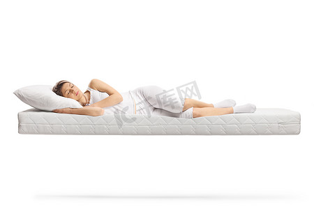 椰棕床垫摄影照片_身穿白色睡衣的年轻女子睡在白色背景的浮动床垫上